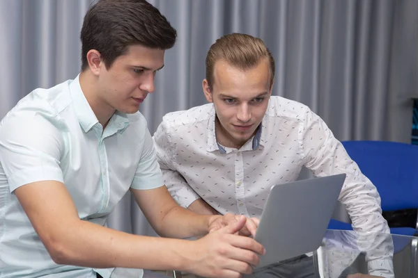 Zwei gut gelaunte junge Geschäftsleute, die zusammen an einem Geschäftstreffen arbeiten und Laptop benutzen — Stockfoto
