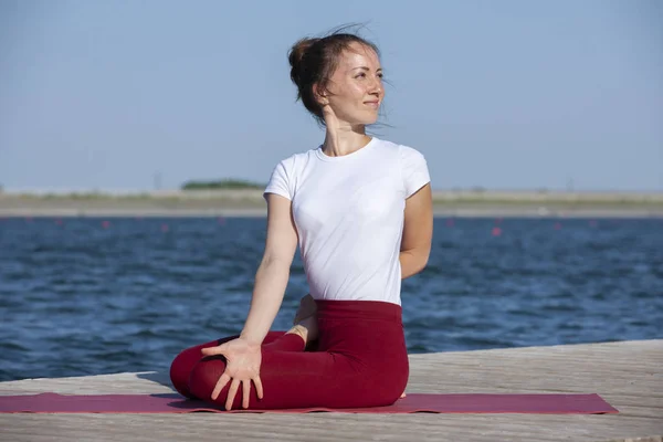 Giovane donna che esercita yoga posa sulla riva del lago al tramonto, ragazza in posa poggiatesta yoga. Le persone viaggiano concetto di relax . — Foto Stock