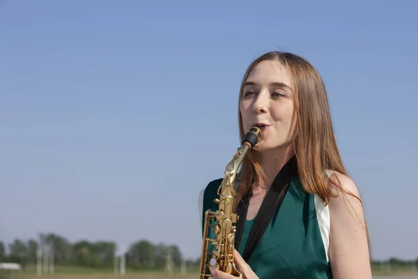 Menina sorridente bonita com saxofone. Jovem saxofonista bonito com saxofone - ao ar livre na natureza . — Fotografia de Stock