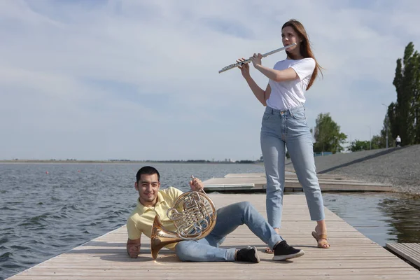 The guy playing the horn and the girl playing the flute on the lake