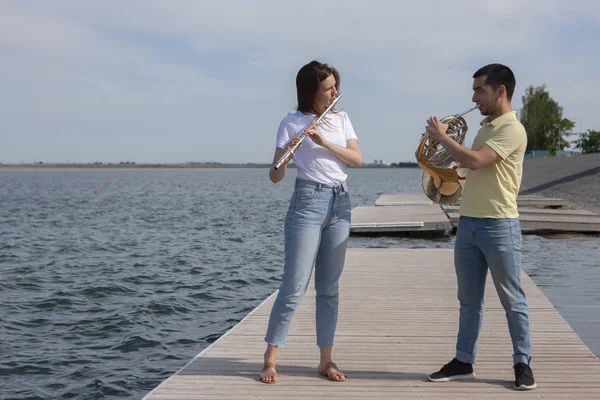 O tipo a tocar trompa e a rapariga a tocar flauta no lago. — Fotografia de Stock