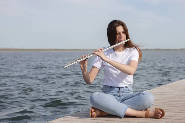 En vacker kvinna poserar i stranden medan du spelar på en flöjt. — Stockfoto