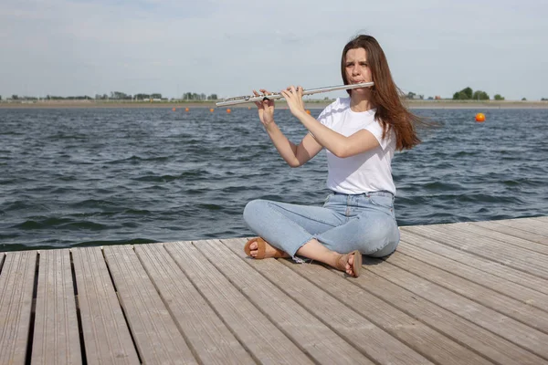 En vacker kvinna poserar i stranden medan du spelar på en flöjt. — Stockfoto