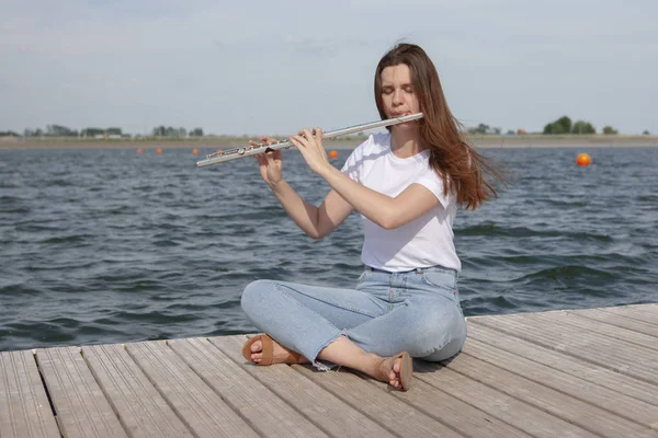 En vacker kvinna poserar i stranden medan du spelar på en flöjt. — Stockfoto