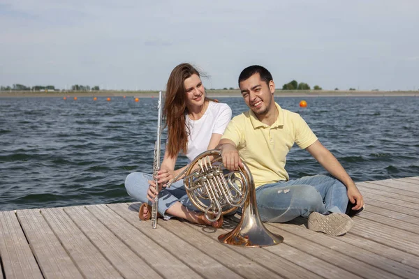 O tipo a tocar trompa e a rapariga a tocar flauta no lago. — Fotografia de Stock