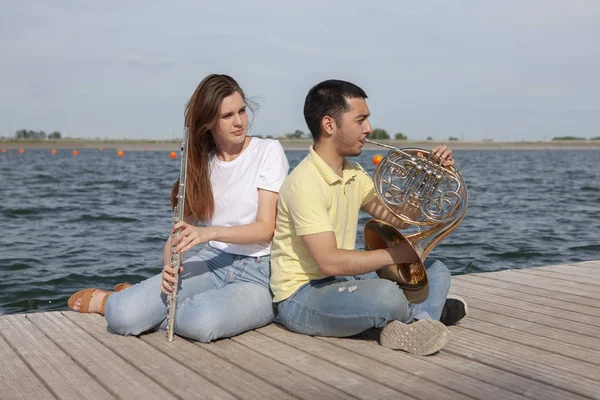 O tipo a tocar trompa e a rapariga a tocar flauta no lago. — Fotografia de Stock