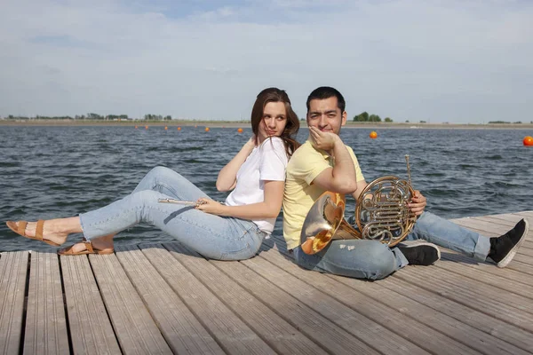 O tipo a tocar trompa e a rapariga a tocar flauta no lago. — Fotografia de Stock