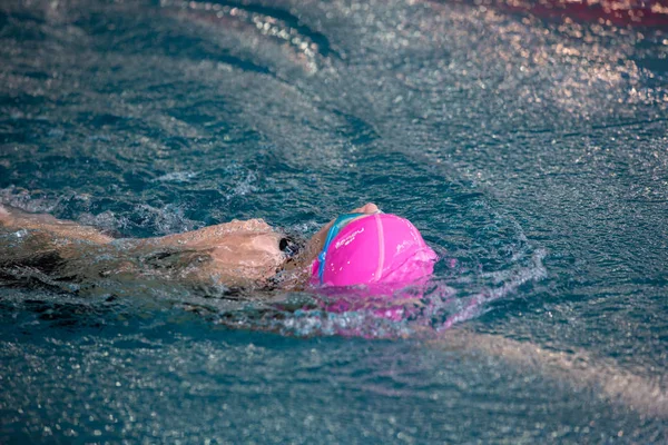 Menina não identificada nadando debaixo de água em uma piscina azul. Imagem abstrata com padrão ondulado de luz solar na água ondulante. Vista superior, cores intensas . — Fotografia de Stock