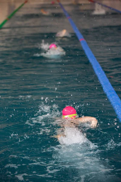 Oidentifierad flicka simning under vatten i en blå pool. Abstrakt bild med vågigt mönster av solljus på porlande vatten. Toppvy, intensiva färger. — Stockfoto