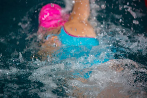 Menina não identificada nadando debaixo de água em uma piscina azul. Imagem abstrata com padrão ondulado de luz solar na água ondulante. Vista superior, cores intensas . — Fotografia de Stock