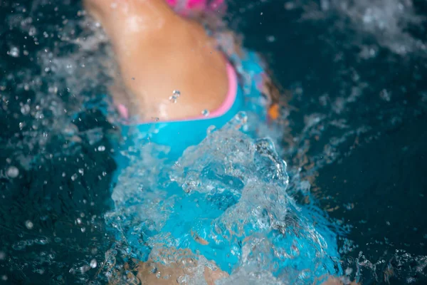 Oidentifierad flicka simning under vatten i en blå pool. Abstrakt bild med vågigt mönster av solljus på porlande vatten. Toppvy, intensiva färger. — Stockfoto