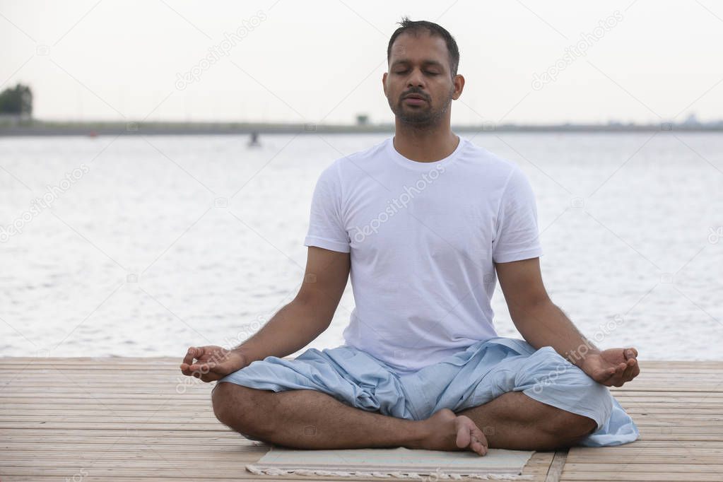 Profile shot of mature man meditating in lotus position on pier against lake