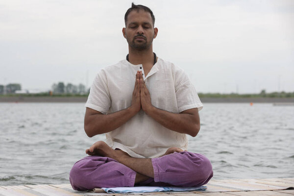 Young man doing yoga and meditating in warrior pose on beach