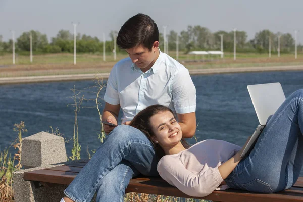 Feliz pareja joven usando el ordenador portátil mientras están sentados juntos en el parque — Foto de Stock