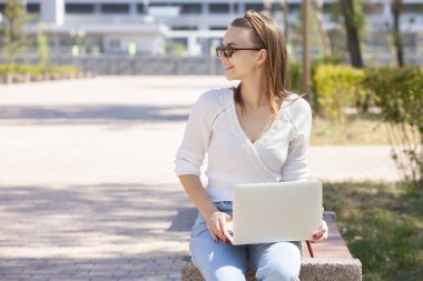 Bir dizüstü bilgisayar ile bir bankta genç kız.