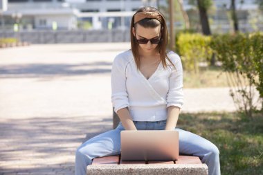 Bir dizüstü bilgisayar ile bir bankta genç kız.