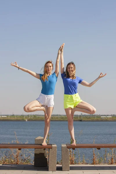 Dos mujeres jóvenes haciendo yoga en la naturaleza. Fitness, deporte, yoga y estilo de vida saludable —  Fotos de Stock