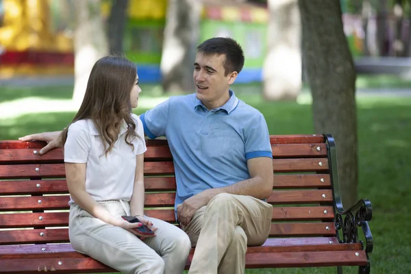 Feliz pareja joven en el amor sentado en un banco del parque y mirando a la cámara — Foto de Stock