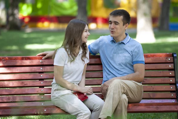 Szczęśliwa Młoda para w miłości, siedząc na ławce w parku i patrząc na kamery — Zdjęcie stockowe