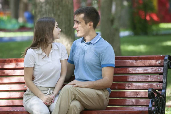 快乐的年轻夫妇，在爱坐在公园的长椅上，看着相机 — 图库照片