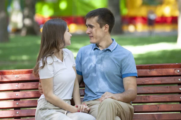 Feliz jovem casal apaixonado sentado em um banco de parque e olhando para a câmera — Fotografia de Stock