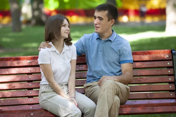 Šťastný mladý pár v lásce sedí na lavičce v parku a při pohledu na fotoaparát — Stock fotografie