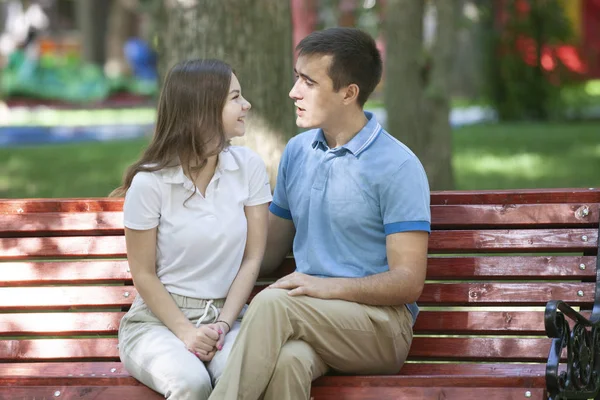 Feliz pareja joven en el amor sentado en un banco del parque y mirando a la cámara — Foto de Stock