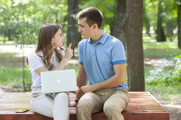 Pareja joven sentados juntos en el banco en el parque y el uso de ordenador portátil — Foto de Stock