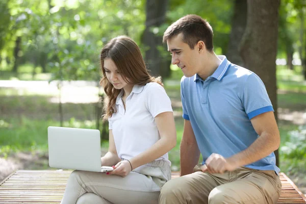 Junges Paar sitzt zusammen auf Bank im Park und benutzt Laptop — Stockfoto