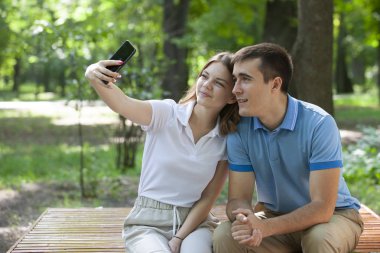 Çift bir parkta bir bankta oturan bir akıllı telefon medya paylaşımı.