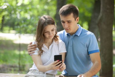 Çift bir parkta bir bankta oturan bir akıllı telefon medya paylaşımı.