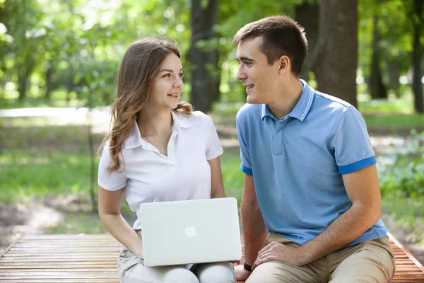 Junges Paar sitzt zusammen auf Bank im Park und benutzt Laptop — Stockfoto