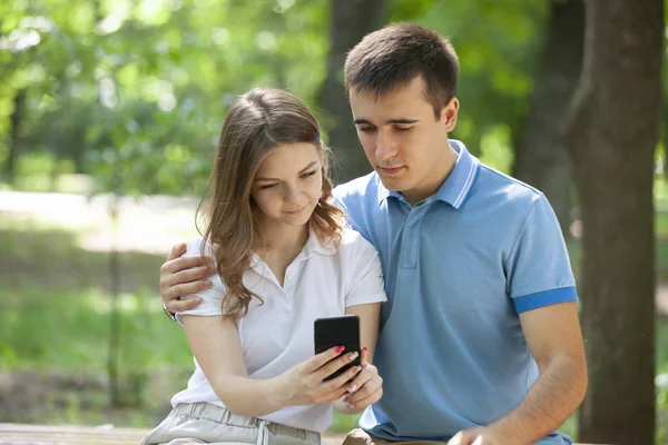 Pareja compartiendo medios en un teléfono inteligente sentado en un banco en un parque . — Foto de Stock