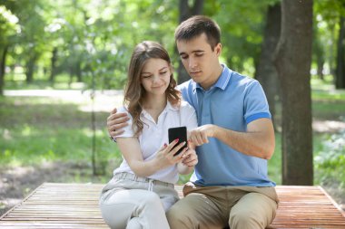 Çift bir parkta bir bankta oturan bir akıllı telefon medya paylaşımı.