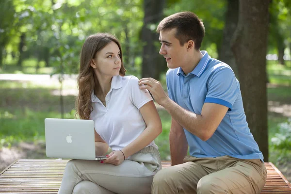 Jovem casal sentado no banco no parque e usando laptop — Fotografia de Stock