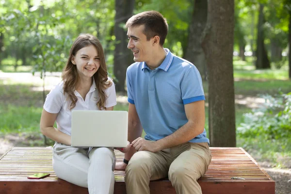 Genç çift parkta bankta birlikte oturan ve dizüstü bilgisayar kullanarak — Stok fotoğraf