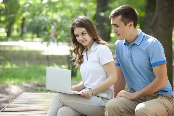 Jovem casal sentado no banco no parque e usando laptop — Fotografia de Stock