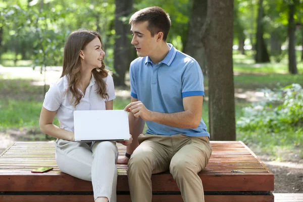 Jovem casal sentado no banco no parque e usando laptop — Fotografia de Stock