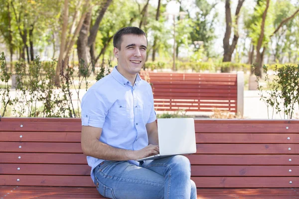 Joven con portátil sentado en un banco de madera — Foto de Stock