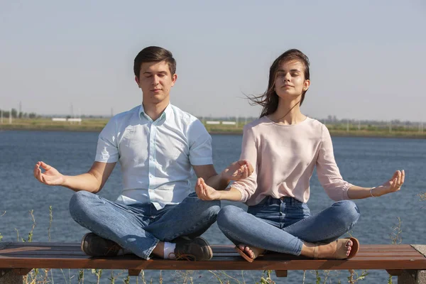 Morning meditation. Beautiful young couple in white clothing meditating outdoors together and keeping eyes closed