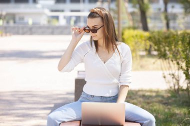 Bir dizüstü bilgisayar kullanarak bir bankta oturan güzel kadın.