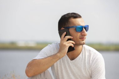 Tezgah açık havada üzerinde oturan ve smartphone kullanarak mutlu genç yakışıklı adam