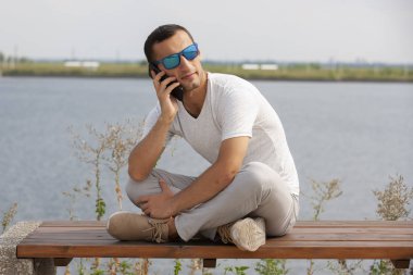 Tezgah açık havada üzerinde oturan ve smartphone kullanarak mutlu genç yakışıklı adam
