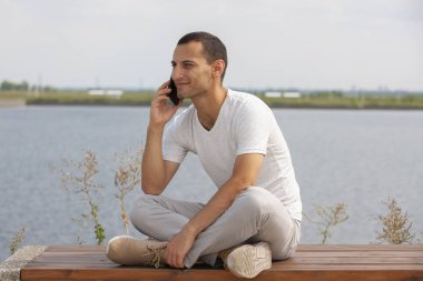 Tezgah açık havada üzerinde oturan ve smartphone kullanarak mutlu genç yakışıklı adam