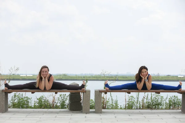 Zwei fröhlich lächelnde blonde Mädchen beim morgendlichen Yoga in der wunderschönen Gebirgsseenlandschaft. Yoga-Rückzug, Sport im Freien — Stockfoto