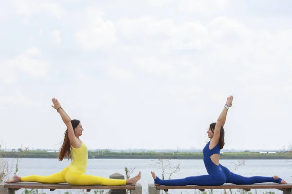 Due ragazze bionde sorridenti felici che fanno l'esercitazione di yoga insieme nella mattina nel paesaggio bello del lago della montagna. Ritiro di yoga, sport all'aperto — Foto Stock