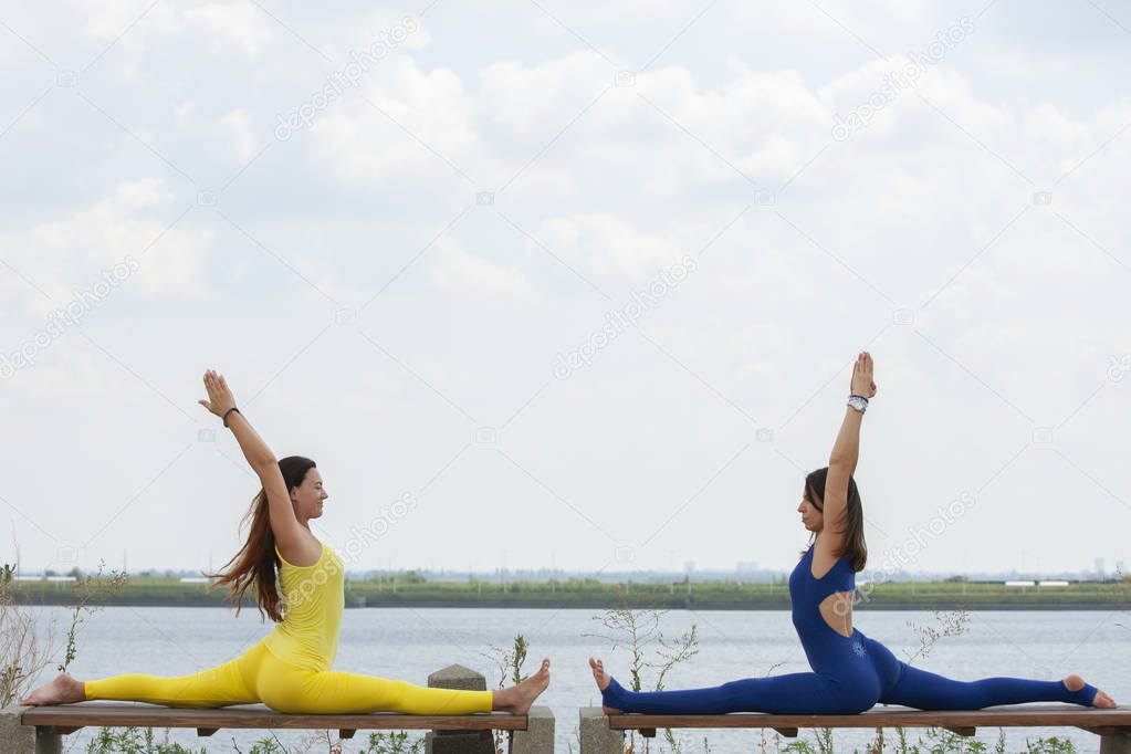 Two happy smiling blond girls doing yoga exercise together in morning in beautiful mountain lake landscape. Yoga retreat, sport outdoor