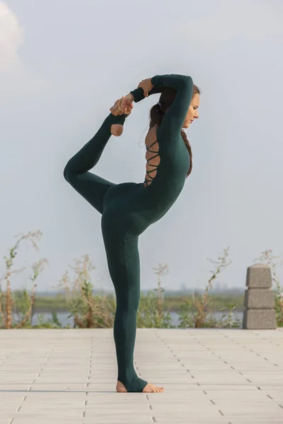 Thin brunette girl plays sports and performs beautiful and sophisticated yoga poses in a summer park. — Stock Photo, Image