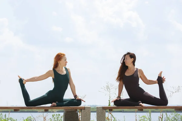 Zwei hübsche Frauen dehnen sich in einem Park, bevor sie eine Trainingseinheit beginnen - Mädchen turnen im Freien — Stockfoto