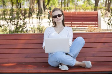 Bir dizüstü bilgisayar ile bir bankta genç kız.